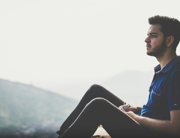 a man sitting on a ledge with a mountain in the background